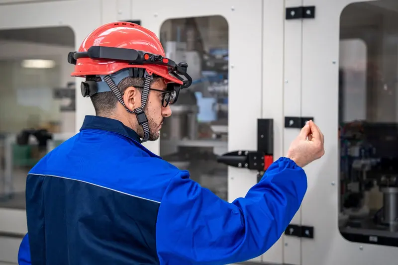 Technician in a safety helmet with a head-mounted mixed reality display operating an industrial machine