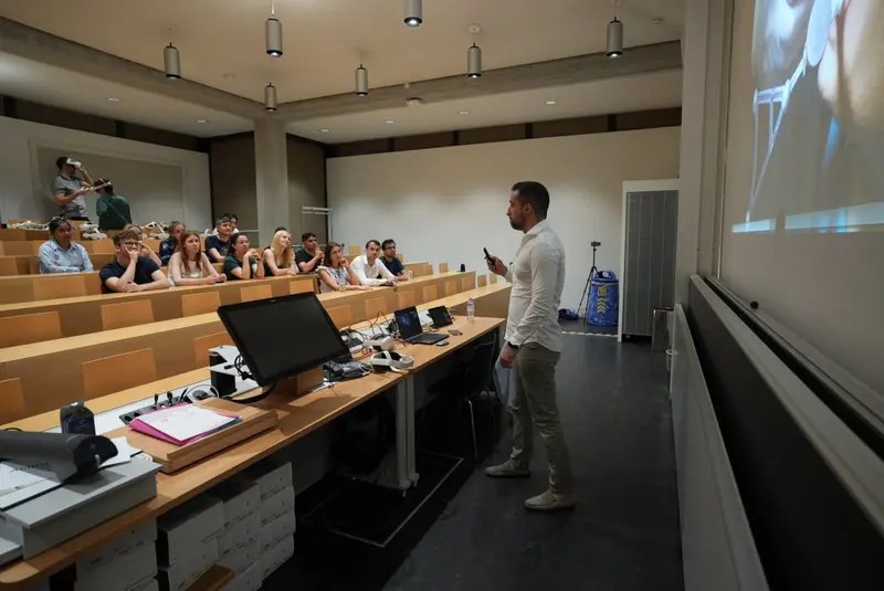 Roberto Mangano lecturing in a hall at the University of Zurich, with students and mixed reality headsets in the audience